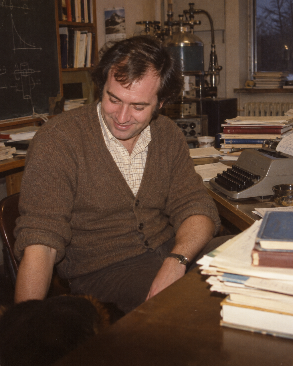 El extraño caso de F. D. C. Willard, coautor de un artículo de física en 1975 3 Físico de los años setenta sentado en un escritorio con una máquina de escribir y revistas apiladas, mirando hacia algo fuera de cuadro con una sonrisa leve