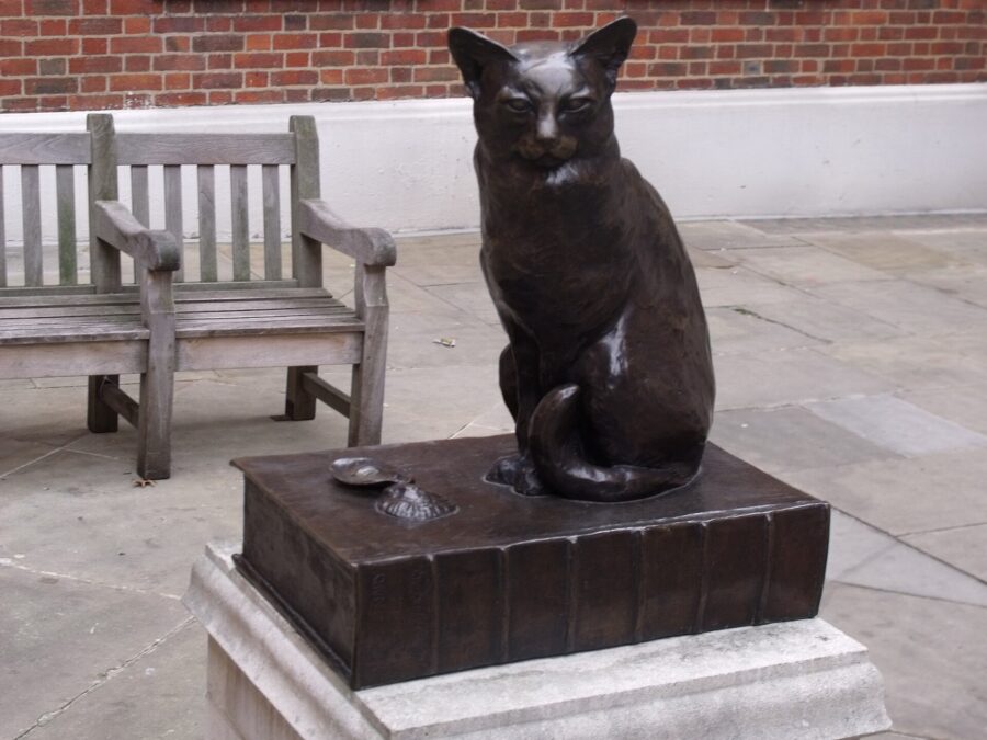 Estatua de bronce de un gato sentado sobre un libro, junto a dos conchas de ostra