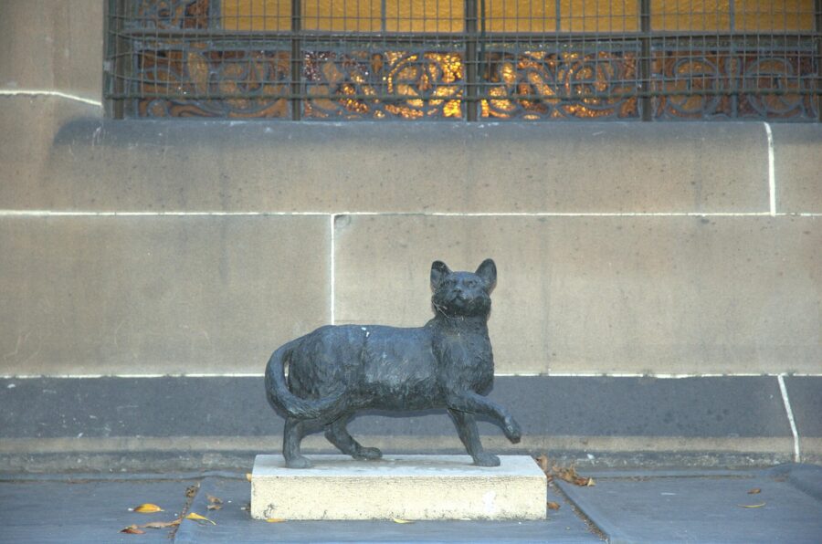 Estatua de bronce de un gato sobre el alféizar de una ventana de piedra