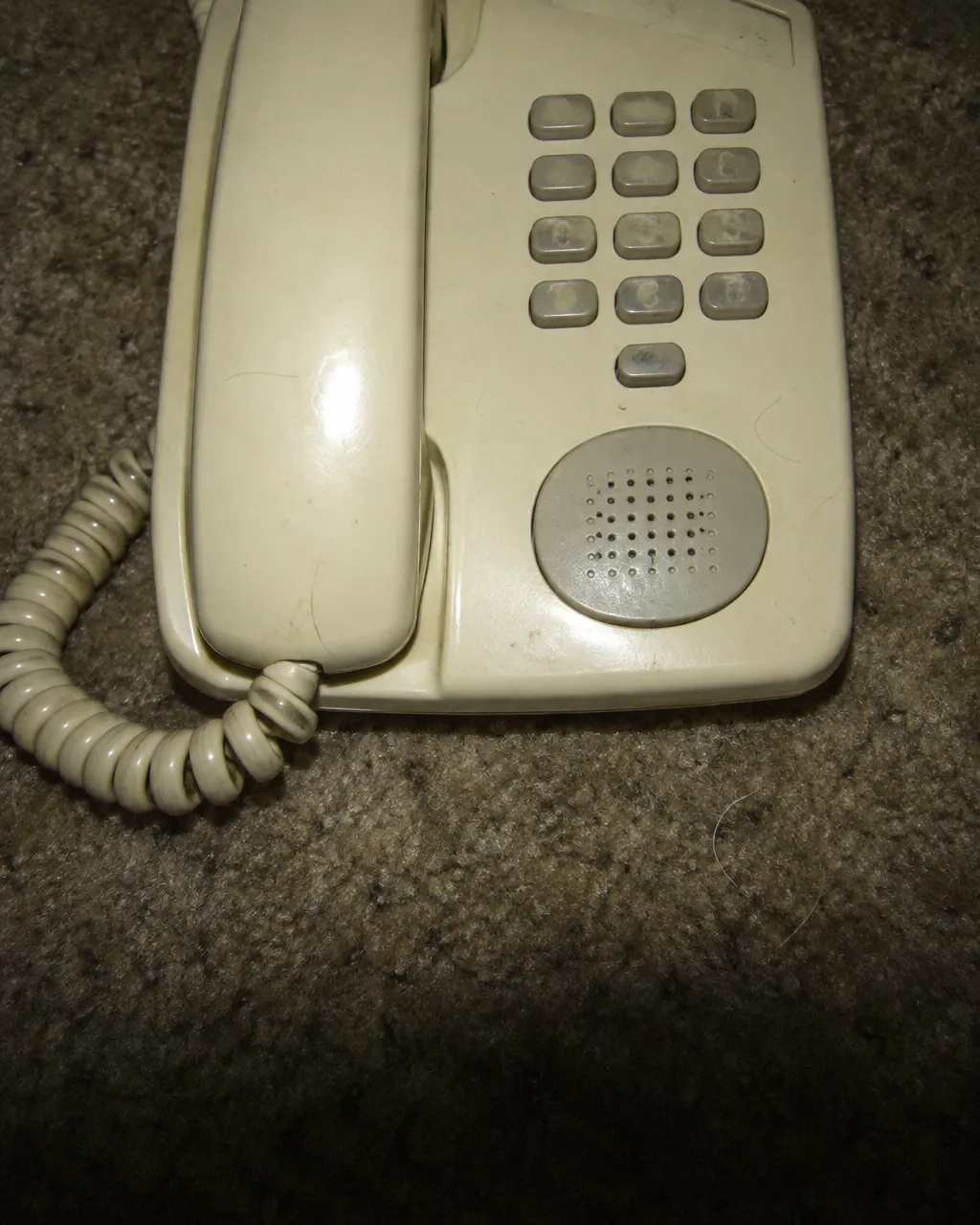 Un hombre no podía levantarse, y el rastro de la llamada a emergencias terminó en su gato 3 Teléfono beige con altavoz, visto desde arriba sobre una alfombra gastada, con un teclado de 12 botones pequeños