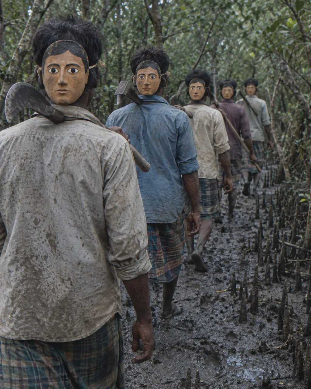 Una cara de goma en la nuca: el plan para engañar al tigre de los Sundarbans 5 Cinco o seis leñadores caminan en fila, de espaldas a la cámara, por un sendero de lodo entre troncos de mangle y raíces que asoman del suelo